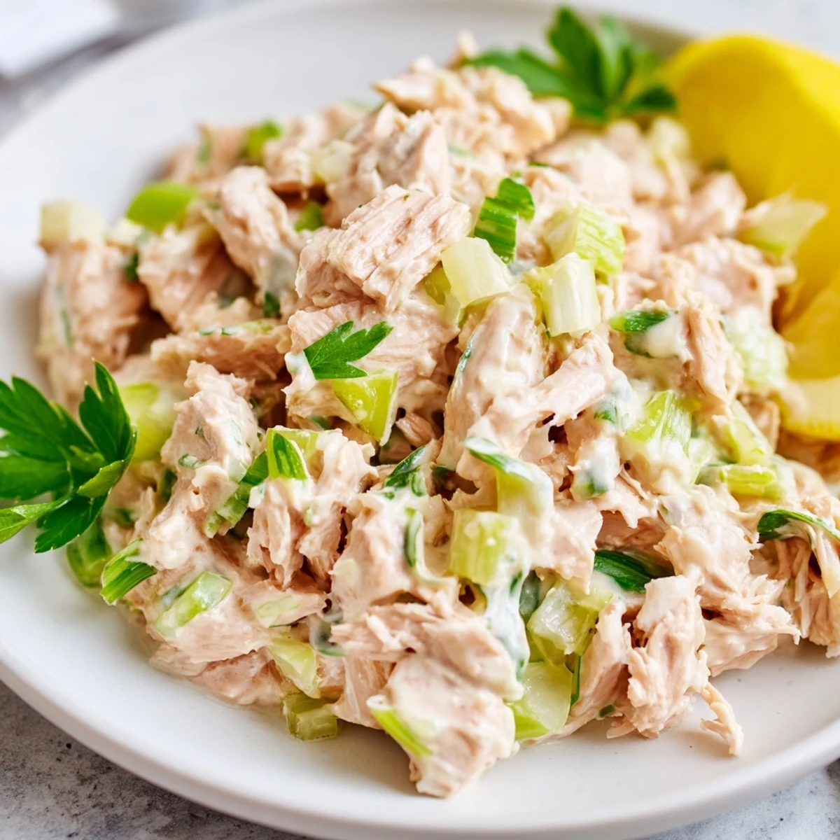 Spicy Zesty Tuna Salad in a white bowl, garnished with fresh parsley and lemon wedges, ready to serve.
