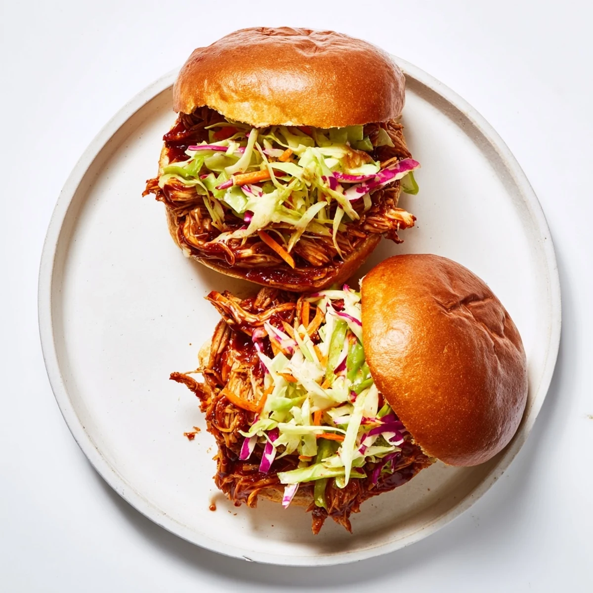Freshly assembled pulled chicken sandwich on a brioche bun, featuring juicy meat and a colorful, tangy slaw topping.