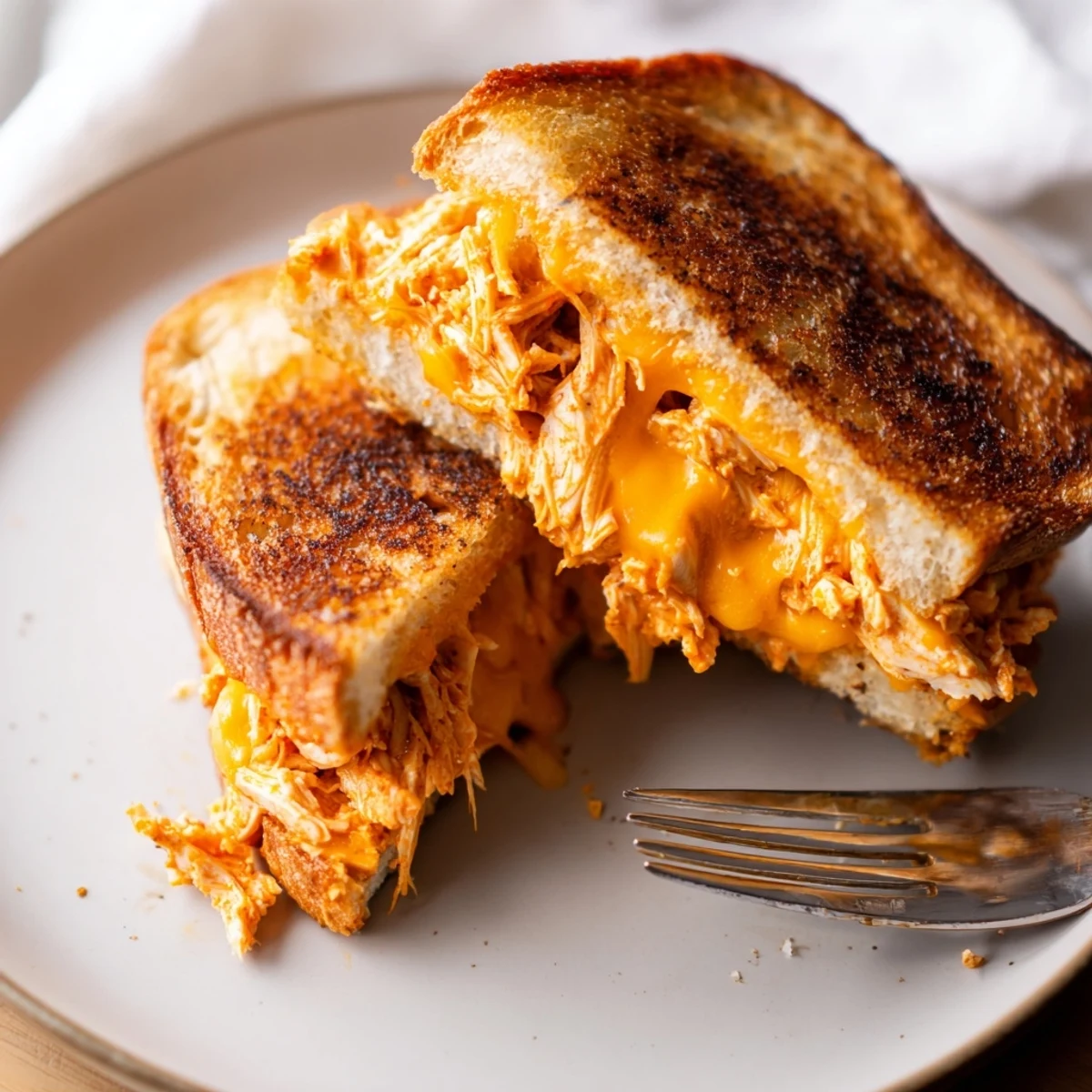 The golden-brown, crispy exterior of a grilled Buffalo Chicken Ranch Grilled Cheese, revealing a juicy, spicy buffalo chicken filling and creamy ranch inside.  