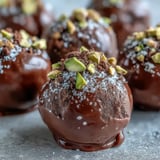 Velvety homemade chocolate truffles coated in chopped pistachios, displayed on a rustic wooden serving board.
