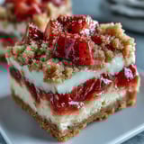 Sliced Strawberry Cheesecake Bars on a white plate with a dollop of whipped cream