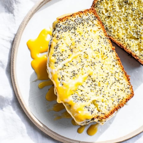 A slice of Glazed Lemon Poppy Seed Cake reveals a moist crumb, topped with a glossy glaze.