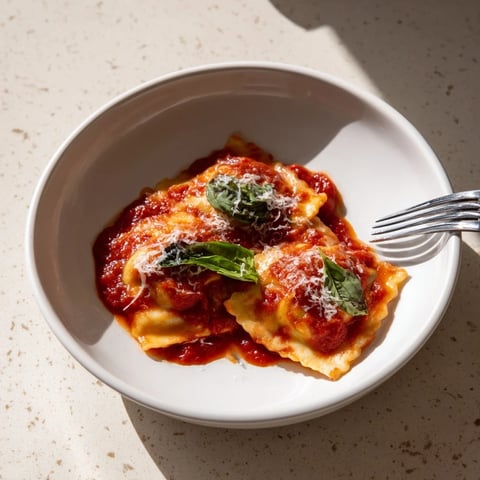Freshly made spinach ricotta ravioli simmering in a rich marinara sauce, topped with basil and Parmesan cheese.