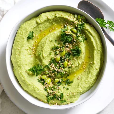 Vibrant Edamame Hummus in a rustic bowl, garnished with fresh parsley and lemon wedges for a bright snack.  