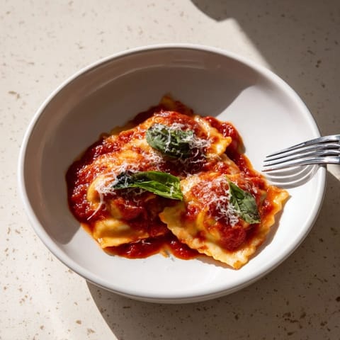 Freshly made spinach ricotta ravioli simmering in a rich marinara sauce, topped with basil and Parmesan cheese.