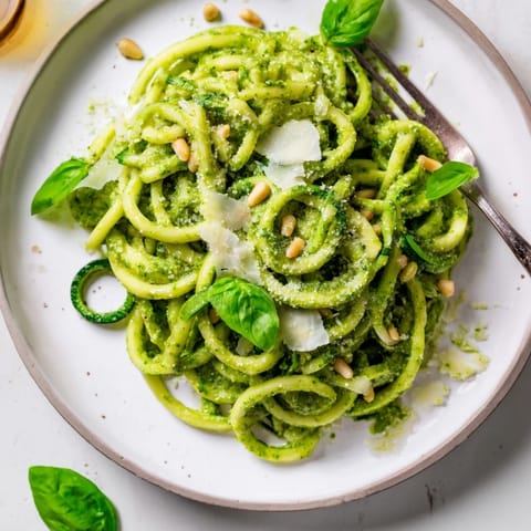 A close-up of homemade basil pesto tossed with spiralized zucchini noodles, garnished with pine nuts and red pepper flakes.  