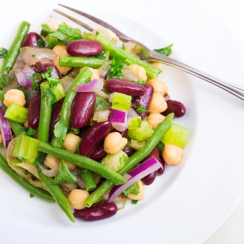 A chilled bowl of Three-Bean Salad with crisp green beans, red kidney beans, and chickpeas in a glistening vinaigrette, ready for a picnic.