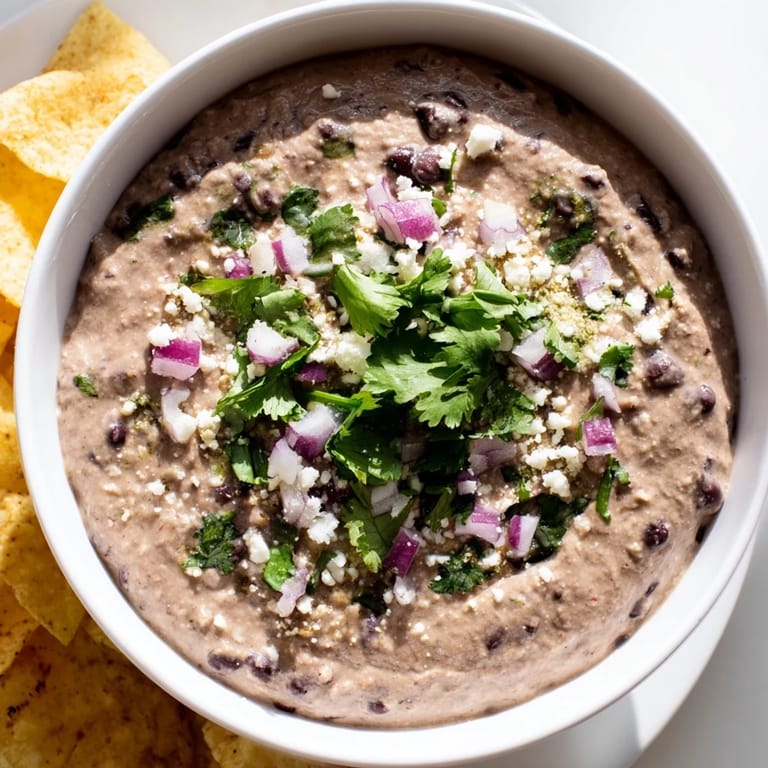 Vibrant bowl of Spicy Black Bean Dip garnished with crumbled cotija and fresh cilantro, perfect for a taco night appetizer.  