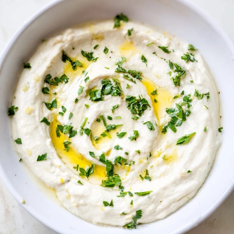 A close-up of velvety white bean dip with a drizzle of olive oil and a lemon wedge nearby for snacking.  