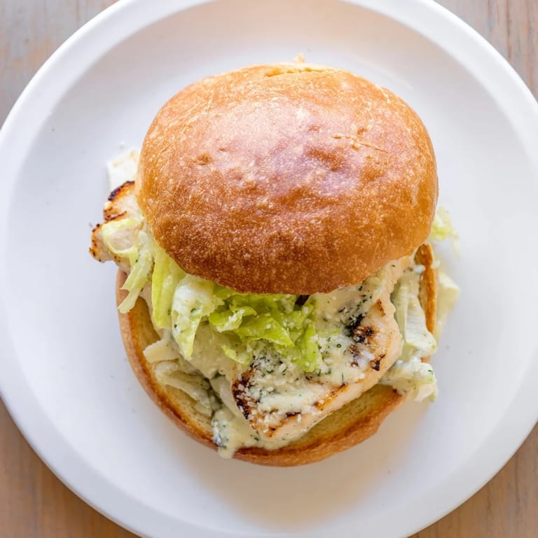 A close-up of a Caesar Chicken Sandwich, revealing juicy layers and fresh greens inside.