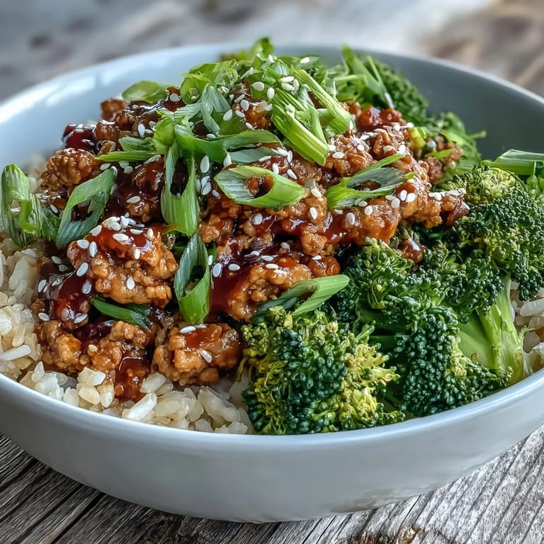 A bowl of sweet and spicy turkey broccoli bowls topped with sesame seeds, green onion, and steamed broccoli. The saucy ground turkey glistens beside nutty brown rice. 