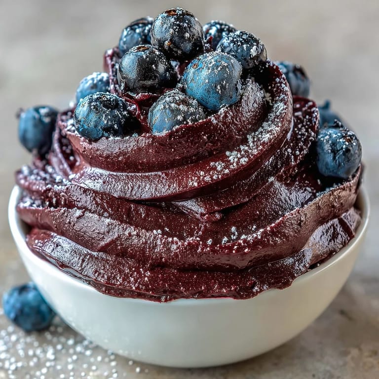Glossy Black Currant Frosting piped high on a vanilla layer cake slice.