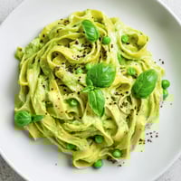 Creamy Green Pea Alfredo served on a white plate, garnished with fresh basil and extra Parmesan.  