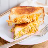 A close-up of Buffalo Chicken Ranch Grilled Cheese, with melted sharp cheddar and spicy buffalo chicken oozing between buttery sourdough slices.  