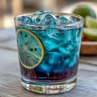 A vibrant glass of butterfly pea flower color-change lemonade, with blue infusion swirling into citrus for a magical purple transformation.